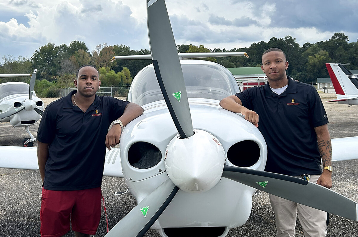 Two students standing beside plane