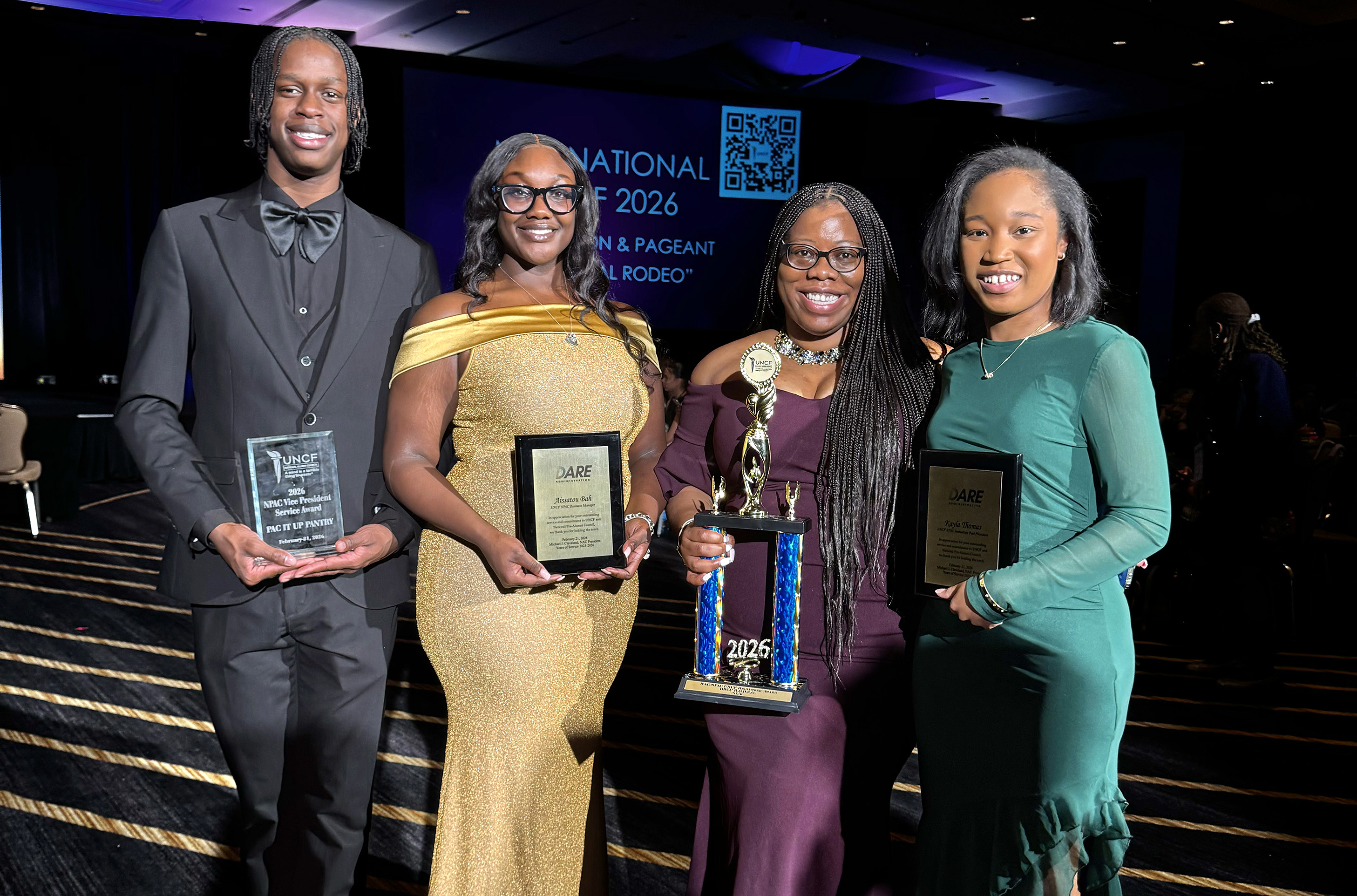 Two students and two alumni holding trophy and awards