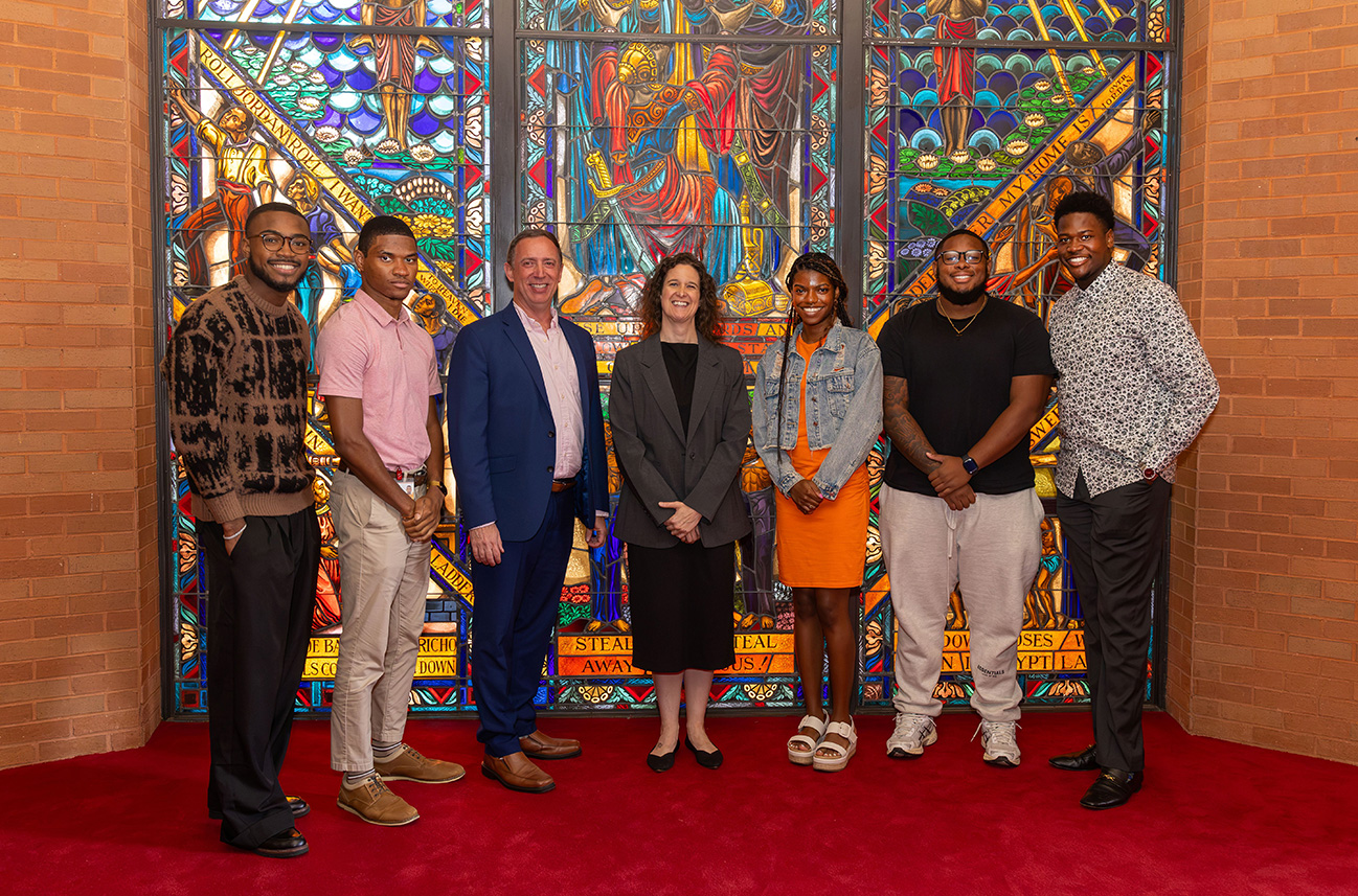 Interfaith America partners pose for a photo with students in front of the famous Singing Windows in the Chapel